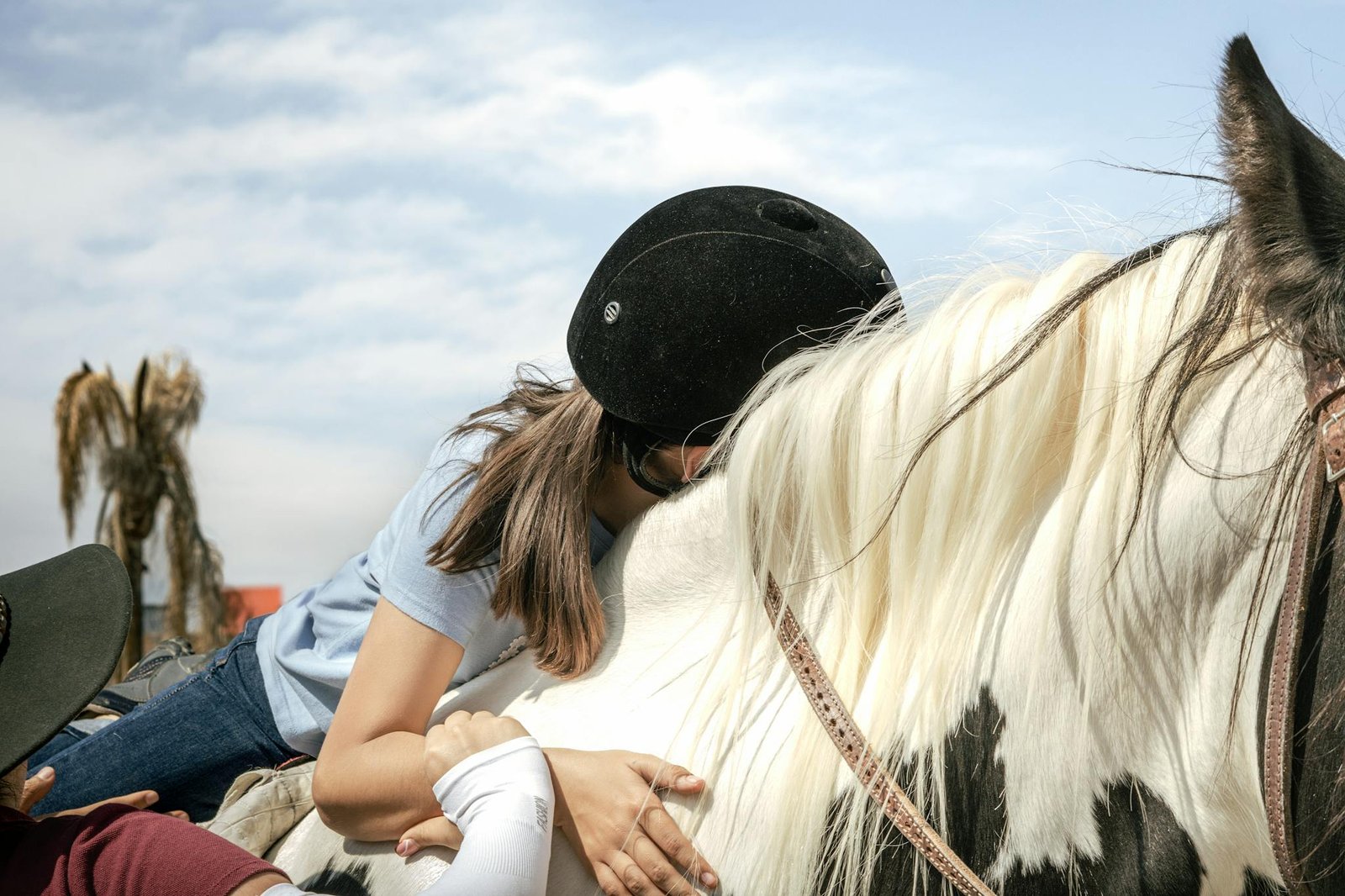 A child participates in equestrian therapy outdoors, shown riding a black and white horse with assistance.