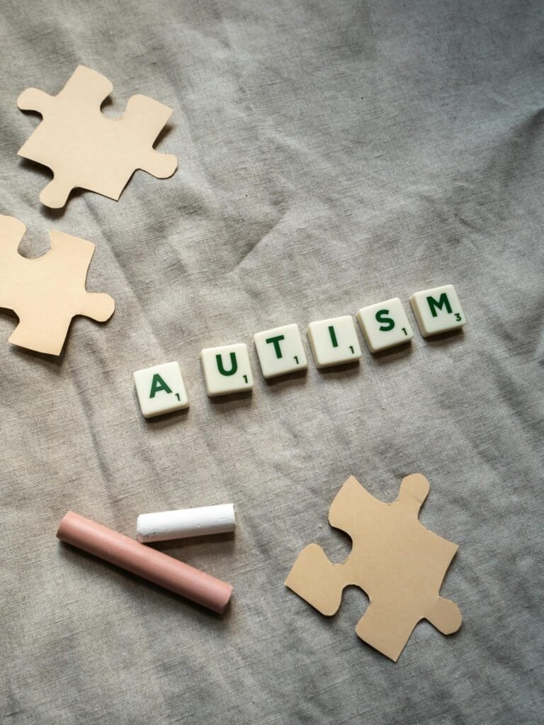 Overhead view of autism spelled with tiles among puzzle pieces on a gray background.
