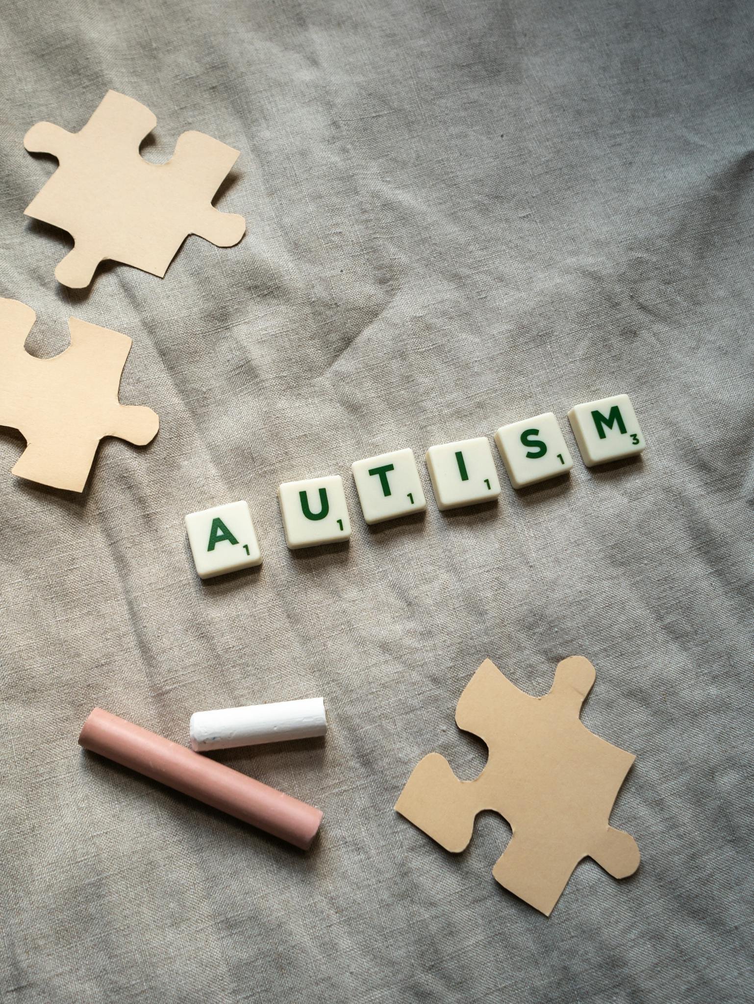Overhead view of autism spelled with tiles among puzzle pieces on a gray background.