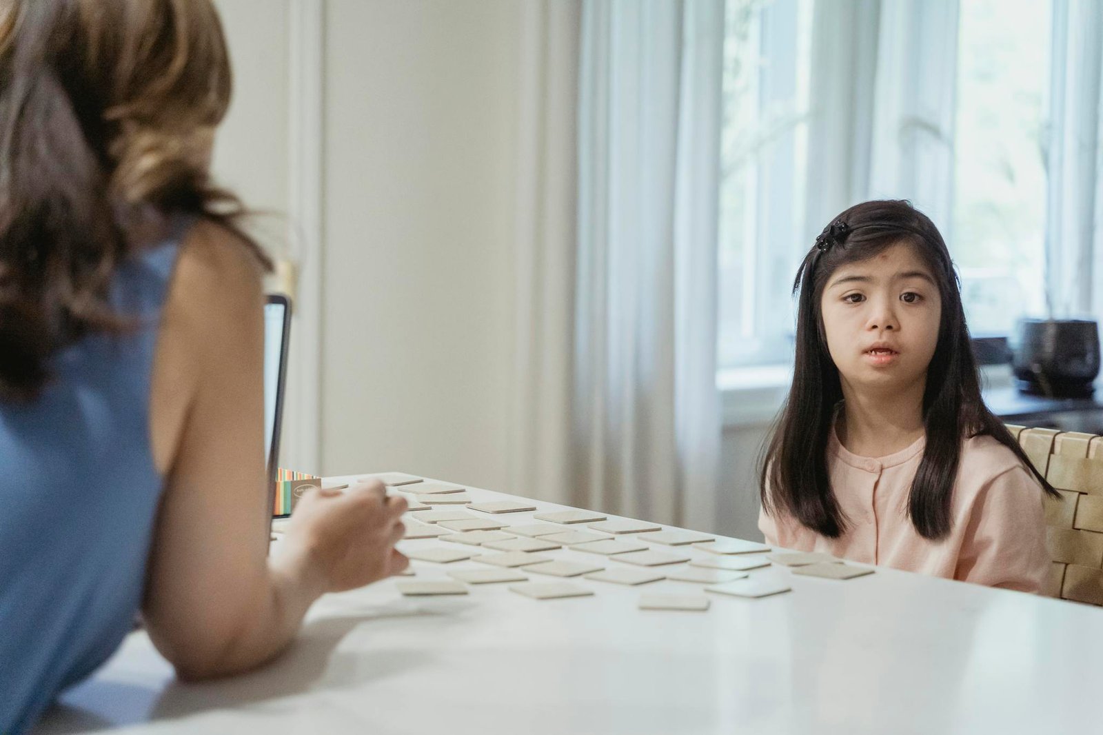 Young girl with Down Syndrome sitting at table playing card game indoors.